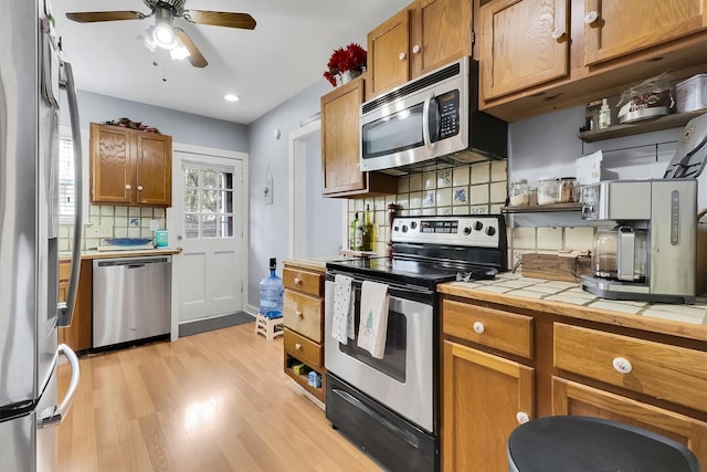 kitchen with appliances with stainless steel finishes, light wood-type flooring, tasteful backsplash, ceiling fan, and tile countertops