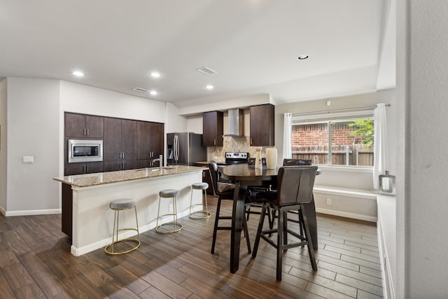 kitchen with stainless steel appliances, dark hardwood / wood-style flooring, dark brown cabinetry, and a breakfast bar