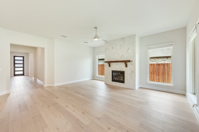 unfurnished living room featuring a fireplace, light wood-type flooring, a healthy amount of sunlight, and ceiling fan