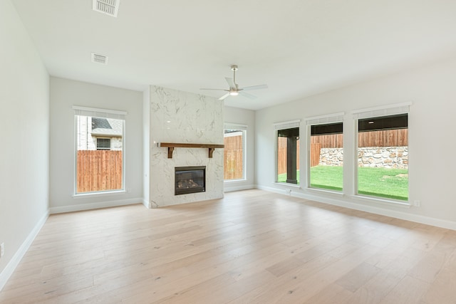 unfurnished living room with light wood-type flooring, a premium fireplace, and ceiling fan