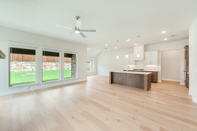 kitchen with light wood-type flooring, white cabinetry, ceiling fan, a center island with sink, and tasteful backsplash