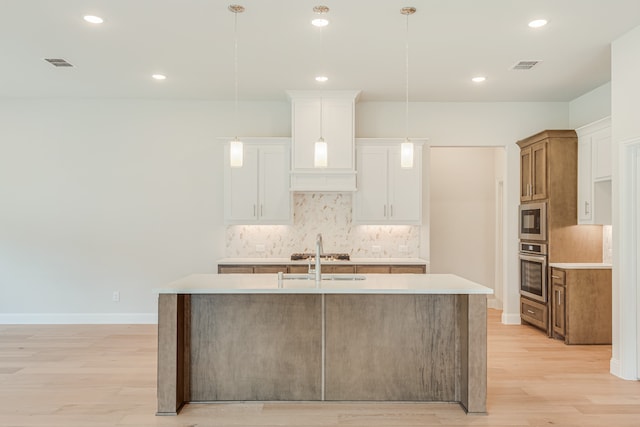 kitchen with white cabinets, light hardwood / wood-style flooring, decorative light fixtures, appliances with stainless steel finishes, and a center island with sink