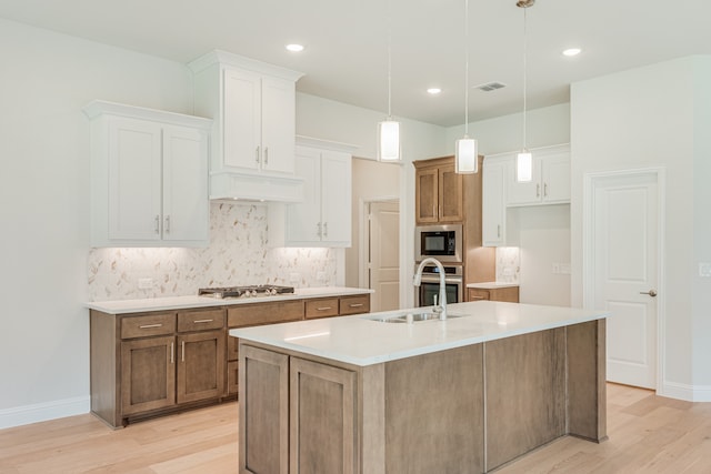 kitchen with hanging light fixtures, light wood-type flooring, appliances with stainless steel finishes, white cabinetry, and a kitchen island with sink