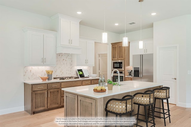 kitchen featuring a kitchen island with sink, light wood-type flooring, stainless steel appliances, and white cabinets