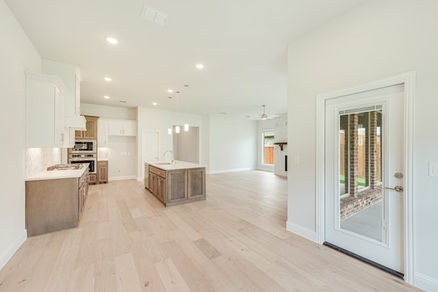 kitchen with hanging light fixtures, oven, sink, ceiling fan, and a kitchen island with sink