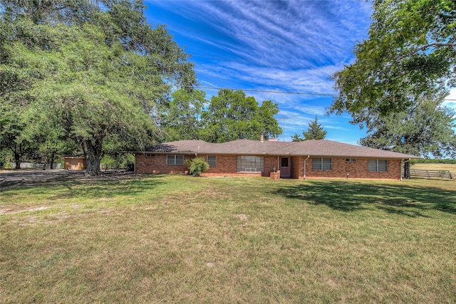 ranch-style home featuring brick siding, a chimney, a front yard, and fence