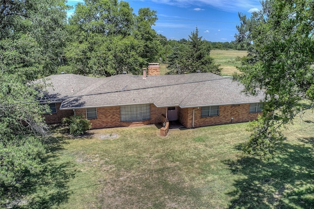 view of front facade featuring brick siding, a chimney, a front yard, and a shingled roof