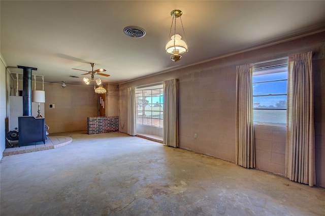 unfurnished living room featuring concrete block wall, visible vents, a ceiling fan, a wood stove, and concrete flooring