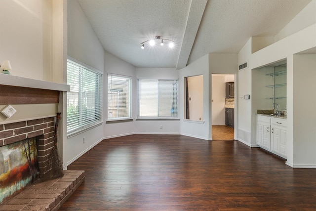 unfurnished living room with lofted ceiling with beams, dark hardwood / wood-style floors, a textured ceiling, and a brick fireplace