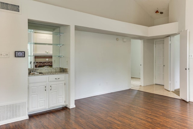 interior space with light stone countertops, sink, hardwood / wood-style flooring, white cabinets, and a high ceiling