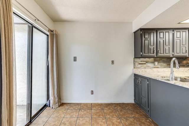 kitchen featuring backsplash, light stone counters, sink, and a textured ceiling