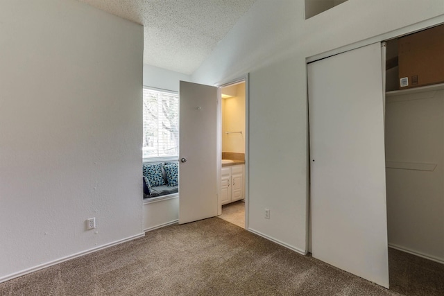 unfurnished bedroom featuring lofted ceiling, light carpet, a textured ceiling, connected bathroom, and a closet