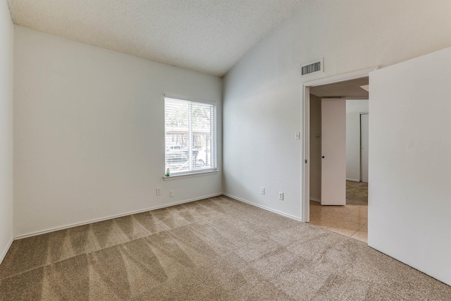 spare room featuring light colored carpet, a textured ceiling, and vaulted ceiling