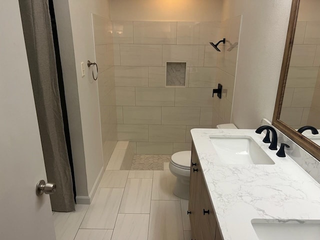 bathroom with tiled shower, vanity, and toilet