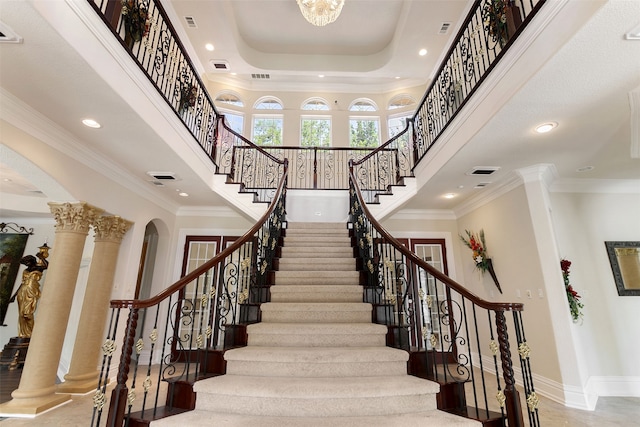 stairs with a towering ceiling, ornate columns, ornamental molding, and a tray ceiling