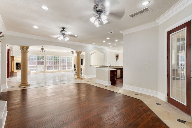 unfurnished living room with ceiling fan, hardwood / wood-style flooring, ornamental molding, ornate columns, and a textured ceiling