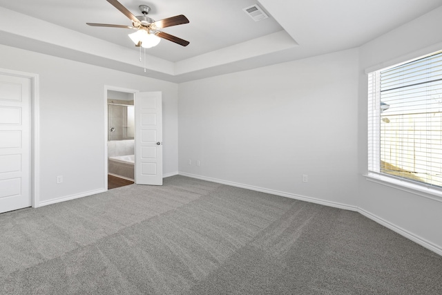 unfurnished bedroom with ceiling fan, multiple windows, ensuite bathroom, and a tray ceiling