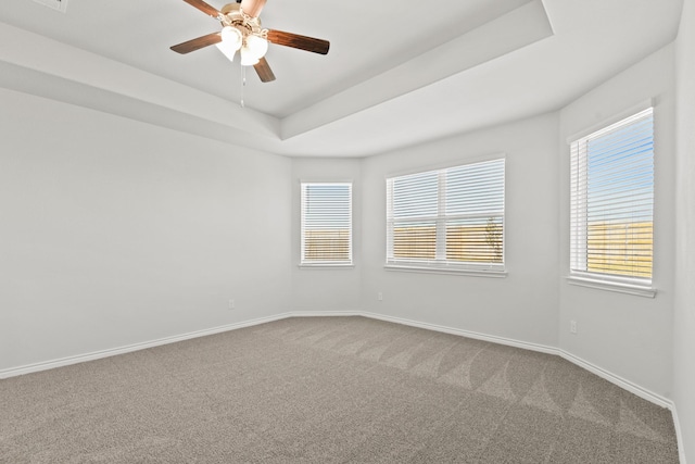 carpeted spare room with a tray ceiling, ceiling fan, and baseboards