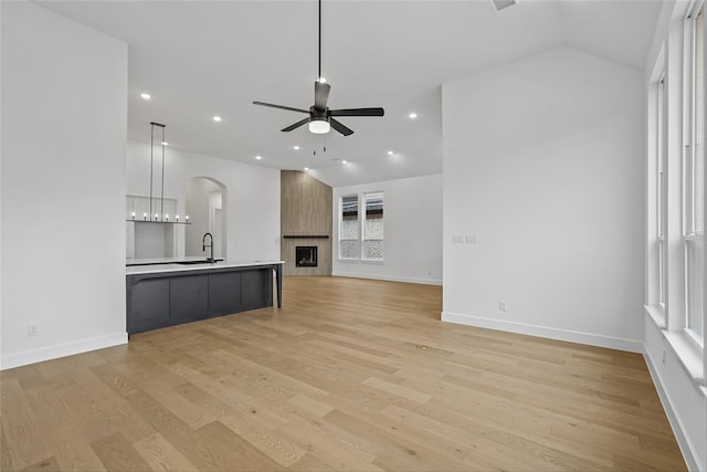 unfurnished living room with a fireplace, light hardwood / wood-style floors, vaulted ceiling, and ceiling fan