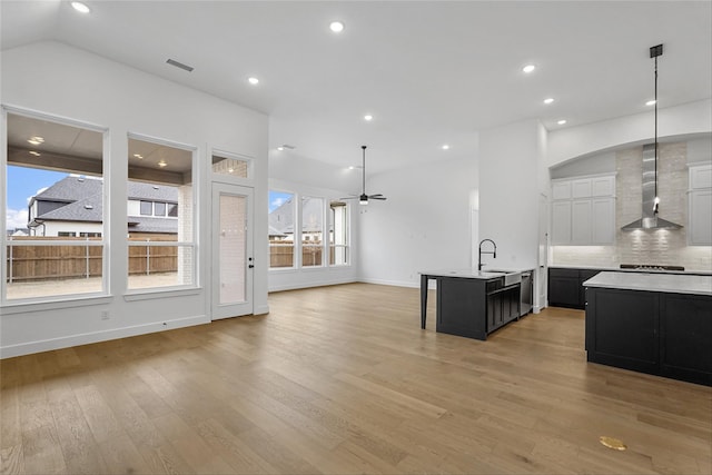 kitchen with wall chimney range hood, a center island with sink, plenty of natural light, and sink