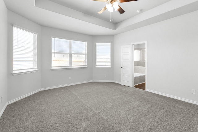 unfurnished bedroom featuring a tray ceiling, ensuite bathroom, carpet flooring, and ceiling fan