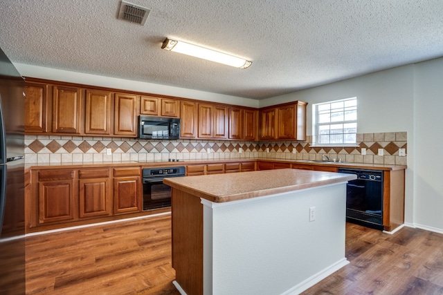 kitchen with a center island, a textured ceiling, black appliances, hardwood / wood-style flooring, and tasteful backsplash