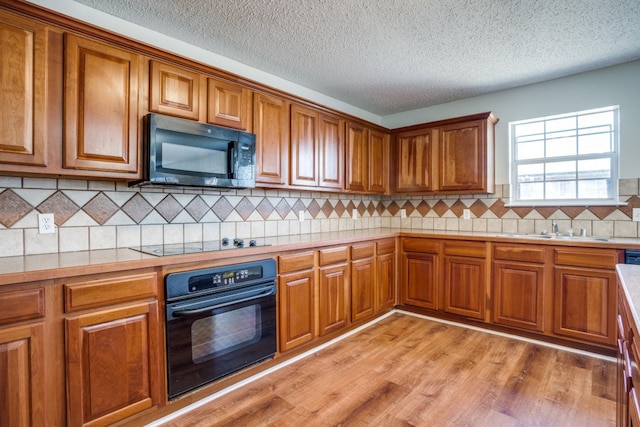 kitchen with light hardwood / wood-style flooring, backsplash, black appliances, sink, and a textured ceiling