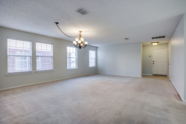 carpeted empty room featuring a chandelier and a textured ceiling