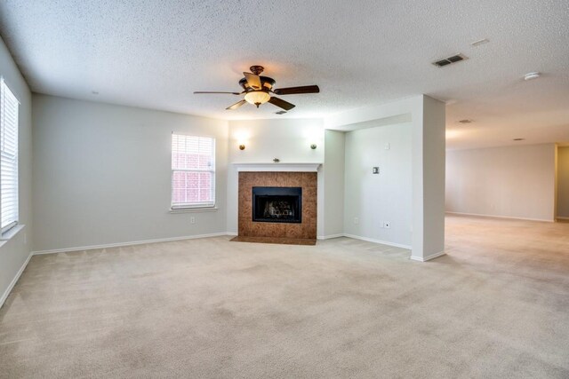 unfurnished living room featuring ceiling fan, a tile fireplace, a textured ceiling, and light colored carpet