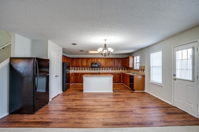 kitchen featuring a notable chandelier, hardwood / wood-style floors, black appliances, a center island, and a textured ceiling