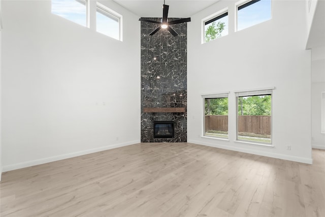 unfurnished living room with a high ceiling, ceiling fan, a large fireplace, and light hardwood / wood-style floors