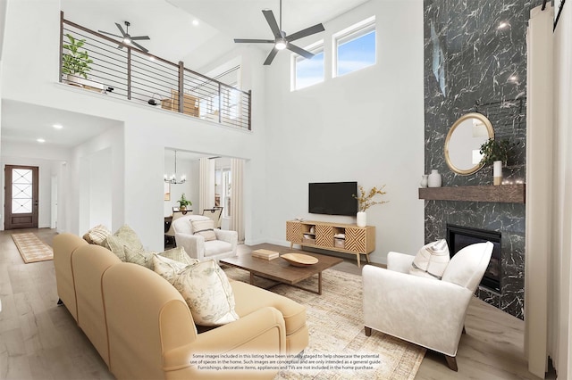 living room featuring a towering ceiling, a high end fireplace, light wood-type flooring, and a healthy amount of sunlight