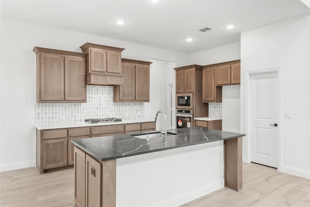 kitchen featuring light hardwood / wood-style flooring, appliances with stainless steel finishes, sink, and a kitchen island with sink