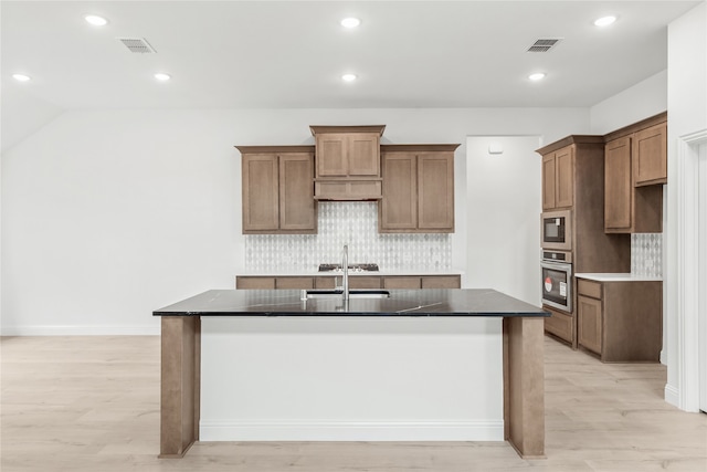 kitchen featuring an island with sink, light hardwood / wood-style floors, stainless steel appliances, and backsplash