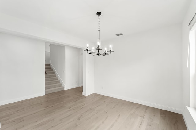 spare room with light wood-type flooring and a notable chandelier