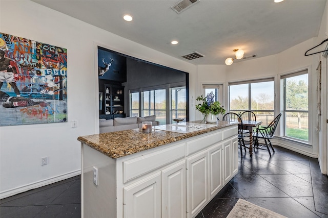 kitchen with light stone countertops, white cabinetry, a kitchen island, and electric stovetop