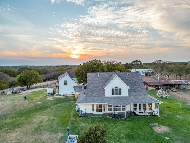 back house at dusk featuring a lawn and a patio