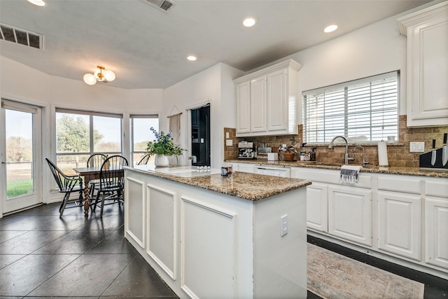 kitchen with white cabinets, a center island, sink, and dark stone counters