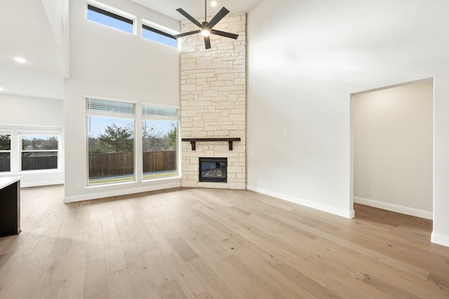 unfurnished living room with a fireplace, a high ceiling, light hardwood / wood-style flooring, and ceiling fan