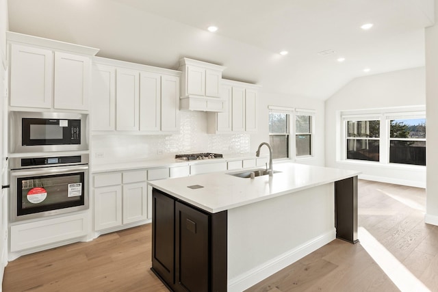 kitchen featuring stainless steel appliances, a kitchen island with sink, sink, white cabinets, and lofted ceiling