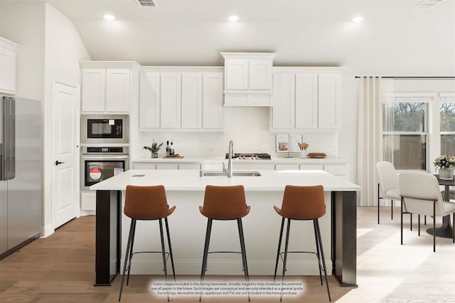 kitchen featuring a kitchen island with sink, appliances with stainless steel finishes, tasteful backsplash, light hardwood / wood-style floors, and white cabinetry