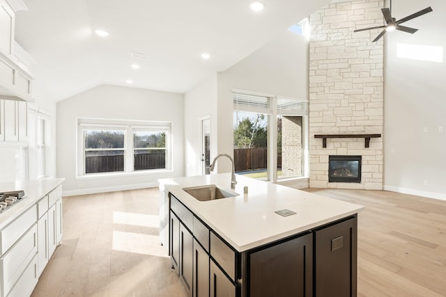 kitchen with dark brown cabinets, sink, light hardwood / wood-style floors, white cabinetry, and a stone fireplace