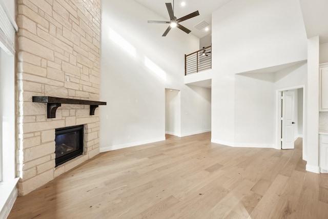 unfurnished living room with ceiling fan, light wood-type flooring, a towering ceiling, and a fireplace