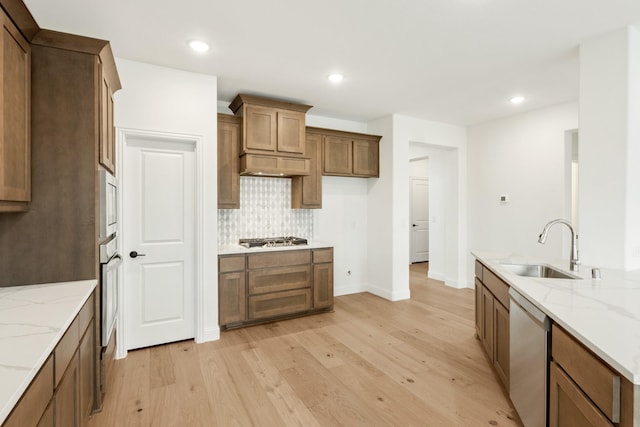 kitchen featuring sink, light hardwood / wood-style flooring, appliances with stainless steel finishes, light stone countertops, and decorative backsplash