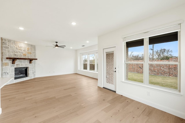 unfurnished living room with a stone fireplace, ceiling fan, and light hardwood / wood-style flooring