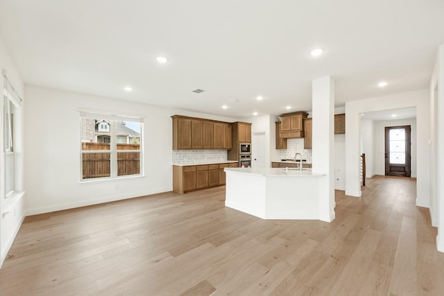 kitchen featuring sink, backsplash, light hardwood / wood-style floors, an island with sink, and oven