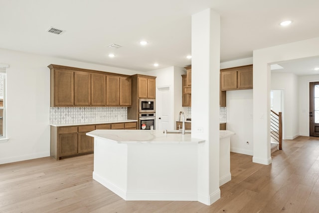 kitchen with built in microwave, stainless steel oven, sink, light hardwood / wood-style floors, and decorative backsplash