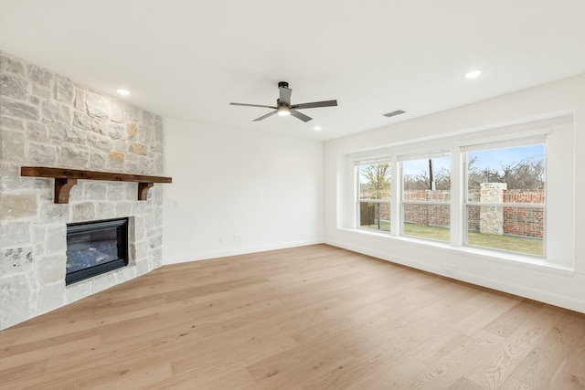 unfurnished living room with light hardwood / wood-style flooring, a stone fireplace, and ceiling fan