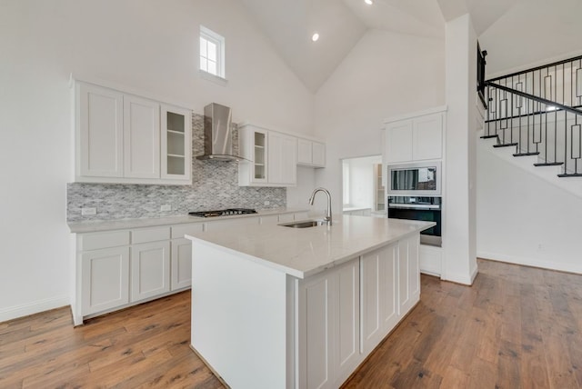 kitchen with a kitchen island with sink, wall chimney range hood, oven, and white cabinetry