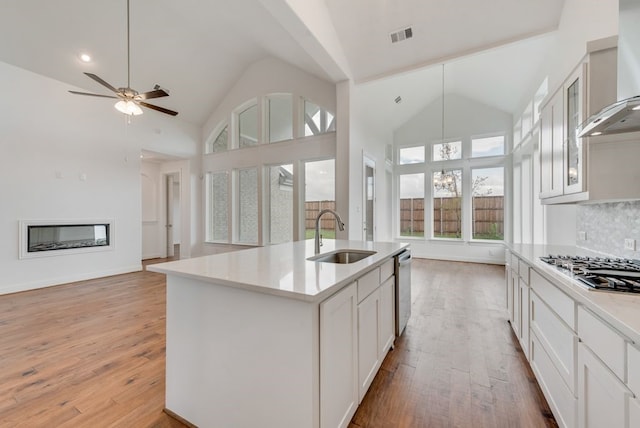 kitchen featuring tasteful backsplash, wall chimney range hood, sink, white cabinetry, and an island with sink